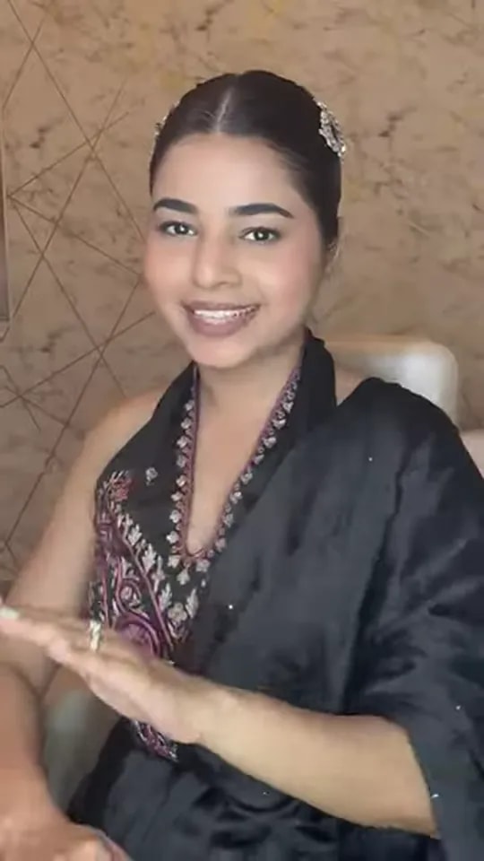 Video thumbnail: smiling presenter in a black embroidered outfit with a sleek bun demonstrating a quick cocktail makeup look