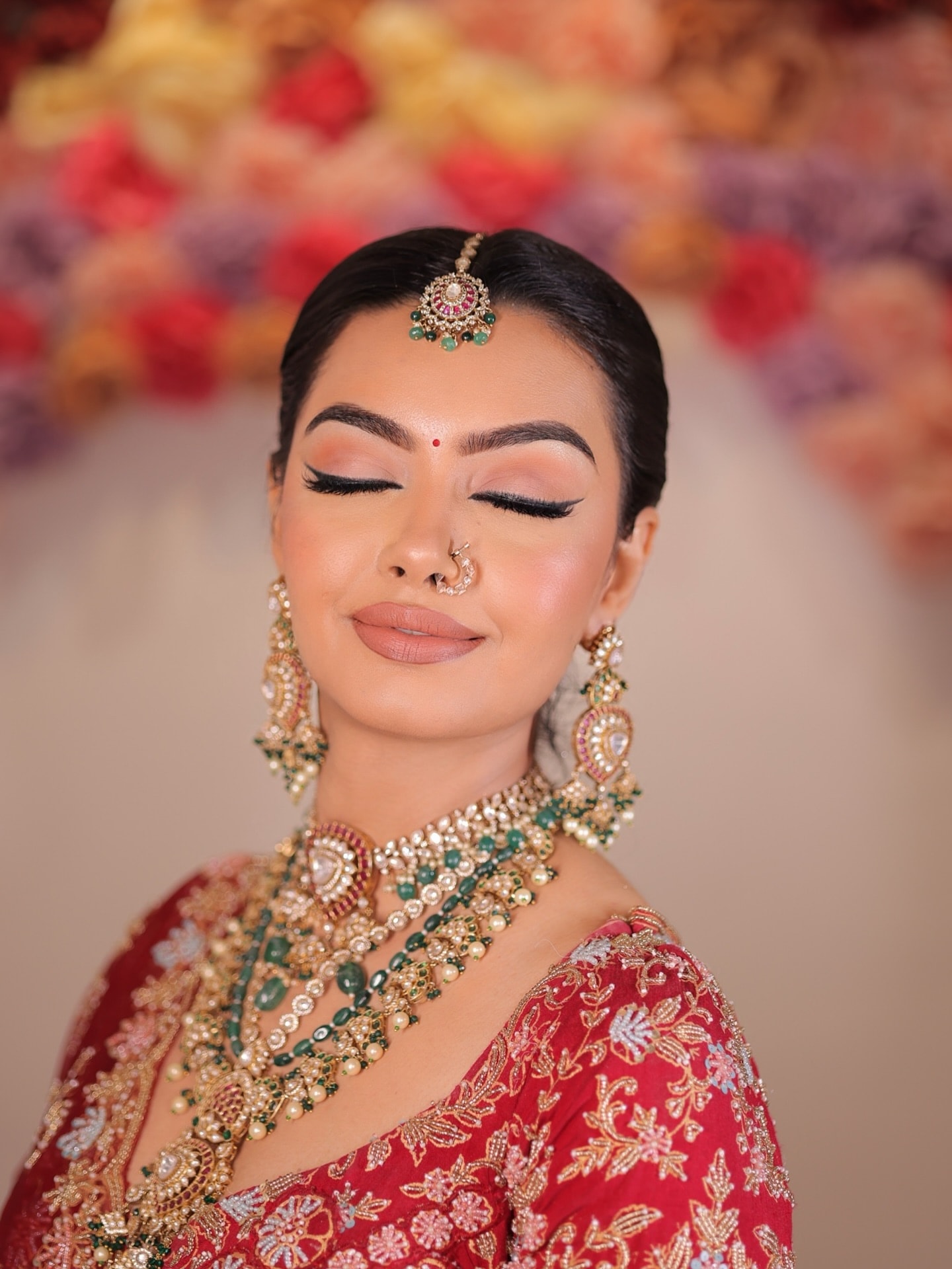 Classic bridal makeup look Classic bridal makeup: bride with eyes closed showing winged liner and peach eyeshadow, red lehenga, kundan and emerald necklace, maang tikka and nath