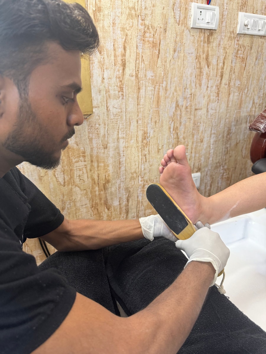 Gloved technician smoothing a client's foot during a pedicure at MG Makeovers