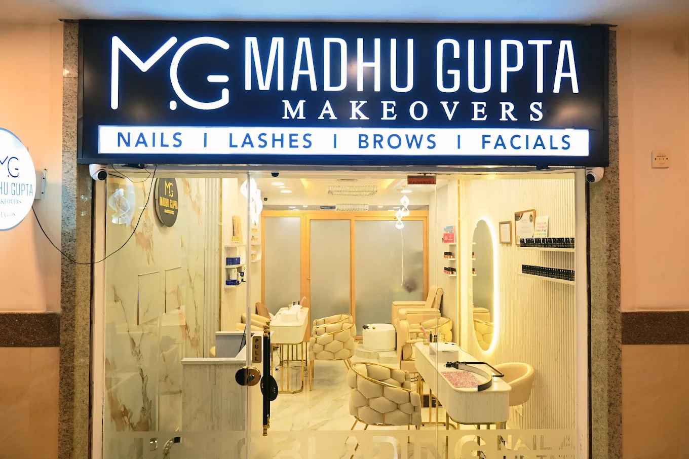 MG Makeovers studio, Mega Mall Lit MG Madhu Gupta Makeovers storefront at Mega Mall, Golf Course Road, Gurugram, signed 'Nails | Lashes | Brows | Facials', with manicure stations inside